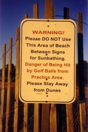 A photo of a sign warning beach goers of a golf practice area.