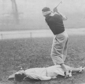 photo of a blindfolded golfer hitting a golf shot from a tee held in a woman's lips.